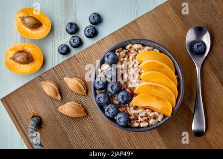 Vollkorn-Haferflocken mit Leinsamen, Heidelbeeren und Aprikosen-Keilen in einer Schüssel auf einem Holztablett Stockfoto