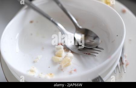 Schmutziges Geschirr aus der Nähe, Löffel, Gabel, Teller mit Speiseresten im Waschbecken Stockfoto