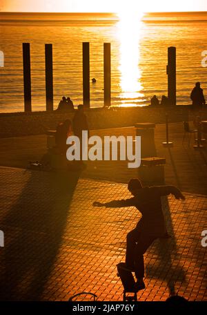 Die Silhouette eines jungen Mannes, der bei Sonnenuntergang neben dem West Pier und i360 auf der unteren Esplanade von Brighton einen Skateboarding-Trick ausführt. Brighton & Hove, Großbritannien Stockfoto