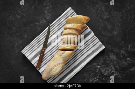 Knusprig frisch geschnittenes Baguette auf Leinenserviette auf dunklem Tisch. Draufsicht. Stockfoto