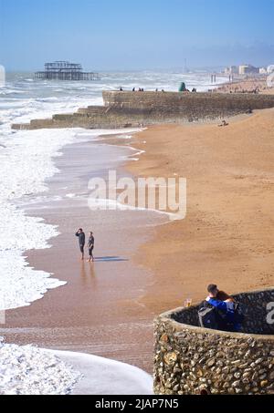 Brighton Beach und die Überreste des West Pier im Hintergrund an einem sonnigen Märztag. Menschen auf der Groyne und Strand dahinter. Brighton, Brighton & Hove, East Sussex, England, Großbritannien Stockfoto