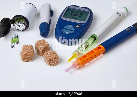 Glucometer, Insulinspritzenstift, brauner Zucker auf einem weißen Tisch. Diabetes-Kontrollkonzept Stockfoto