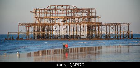 Rostreste des verfallenen West Pier bei Ebbe im Morgengrauen. Brighton & Hove, Sussex, England, Großbritannien. Pärchen, die am Strand spazieren gehen Stockfoto