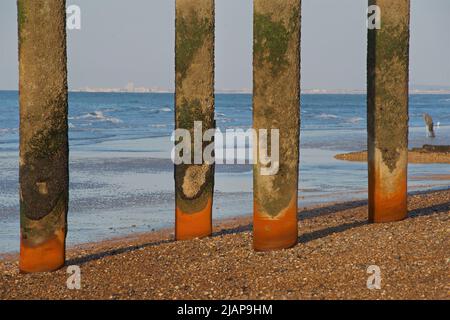 Vier vertikale Eisensäulen erheben sich vom Strand an der Stelle des historischen West Pier-Gebäudes, das nach seiner Schließung im Jahr 1975 verfiel und verloren ging. Gezeiten Niedrig. Brighton, East Sussex, England, Großbritannien. Worthing am fernen Horizont. Stockfoto