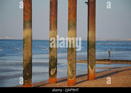 Vier vertikale Eisensäulen erheben sich vom Strand an der Stelle des historischen West Pier-Gebäudes, das nach seiner Schließung im Jahr 1975 verfiel und verloren ging. Gezeiten Niedrig. Brighton, East Sussex, England, Großbritannien. Worthing am fernen Horizont. Stockfoto