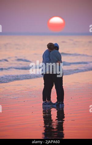 Ein Paar, das sich bei Ebbe, Sonnenuntergang, Brighton, England, Großbritannien, liebevoll am Strand umarmt. Stockfoto