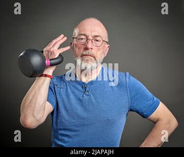 Älterer Mann (Ende 60s) trainiert mit eiserner Kettlebell, aktiver Senior und Fitnesskonzept Stockfoto