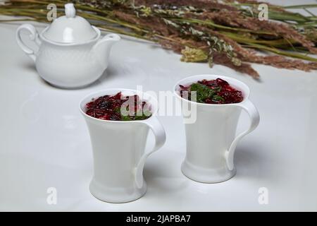 Karcade Kräutertee aus Blumen der sudanesischen Rose und Minze in eleganten weißen Tassen auf einem weißen Tisch vor dem Hintergrund einer Teekanne und eines bou Stockfoto