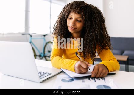 Junge Geschäftsfrau, die vom Home Office aus am Laptop arbeitet Stockfoto