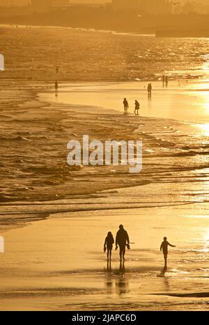 Silhouetten von Menschen, die bei Ebbe am freiliegenden Sandstrand spazieren, Brighton & Hove, East Sussex, England, Großbritannien. Stockfoto