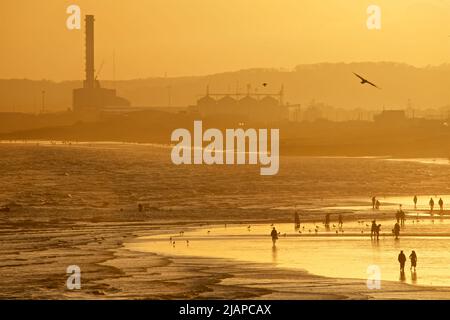 Silhouetten von Menschen am Strand bei Ebbe, Brighton & Hove, East Sussex, England, Großbritannien. Shoreham Power Station in der Ferne. Stockfoto