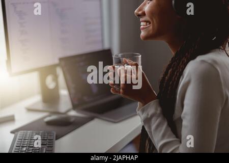 Nahaufnahme einer jungen glücklichen Frau, die lächelt und eine Tasse Tee hält, während sie am Computer arbeitet Stockfoto