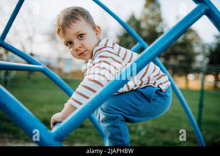 Ein kleiner Junge spielt auf dem Spielplatz im Freien. Stockfoto