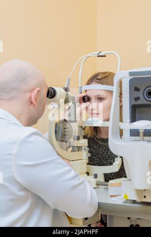 Ein männlicher Augenarzt überprüft das Sehvermögen eines jungen Mädchens mit einem modernen Gerät mit einem Lichtstrahl. Stockfoto