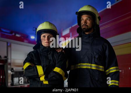 Glückliche Feuerwehrleute Mann und Frau nach der Aktion Blick auf Kamera mit Feuerwehrauto im Hintergrund Stockfoto