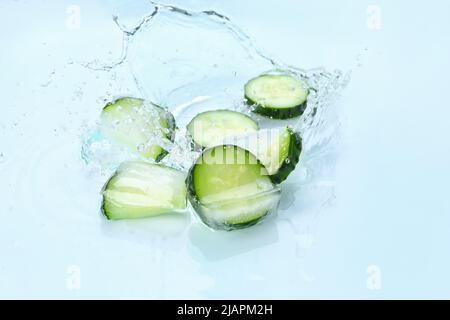 Frische Gurkenscheiben, gefroren in Eis mit Wasserspritzern auf weißem Hintergrund Stockfoto