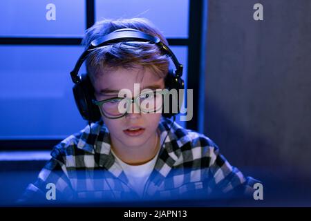 Kleiner Gamer Junge mit Kopfhörern, der Computervideospiel spielt. Stockfoto