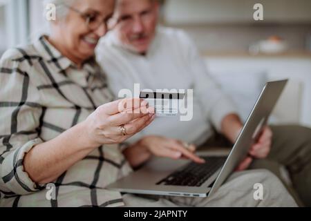 Seniorenpaar sitzt auf dem Sofa und kauft online mit Laptop und Kreditkarte ein Stockfoto