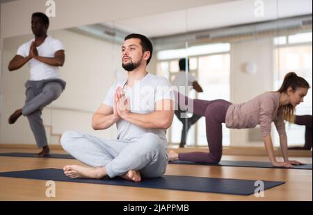 Junger bärtiger Mann, der in Padmasana mit namastigen Händen sitzt Stockfoto