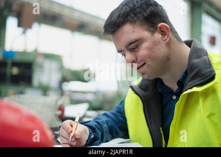 Junger Mann mit Down-Syndrom arbeitet in der industriellen Fabrik, soziale Integration Konzept. Stockfoto