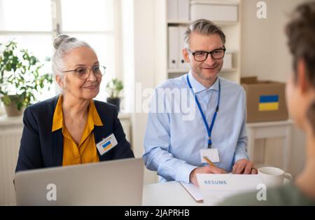 Freiwillige Helferinnen von Frauen und Männern, die der ukrainischen Frau beim Ausfüllen von Formularen im Asylzentrum helfen. Stockfoto