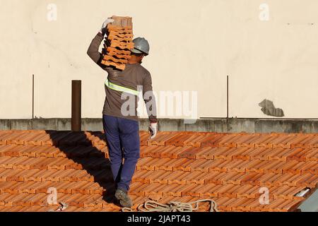 Mann arbeitet an der Dachinstallation. Dachkonstruktion. Reparatur des Ziegeldachs. Haus im Bau. Arbeiter renoviert Abdichtung Dach des Gebäudes. Stockfoto