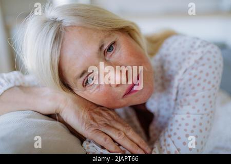 Porträt einer traurigen attraktiven älteren Frau, die zu Hause auf einem Sofa sitzt und nachdenklich ist. Stockfoto