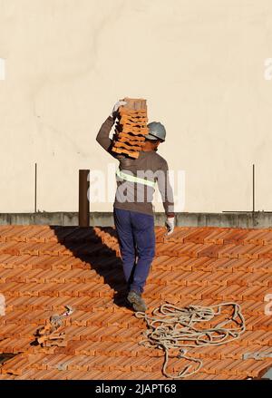 Mann arbeitet an der Dachinstallation. Dachkonstruktion. Reparatur des Ziegeldachs. Haus im Bau. Arbeiter renoviert Abdichtung Dach des Gebäudes. Stockfoto