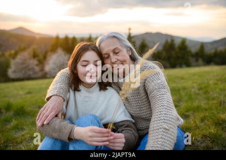 Glückliche ältere Großmutter mit Teenager-Großdaguhter, die sich am Frühlingstag in der Natur umarmt. Stockfoto