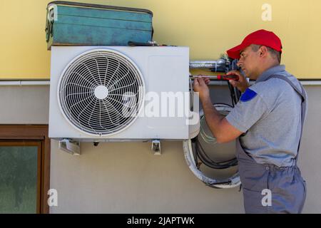 Bild eines Klempners mit Werkzeugen, die eine Klimaanlage in einem Haus installieren. Hinweis auf die bevorstehende Hitze Stockfoto