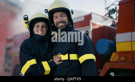 Glückliche Feuerwehrleute Mann und Frau nach der Aktion Blick auf Kamera mit Feuerwehrauto im Hintergrund Stockfoto