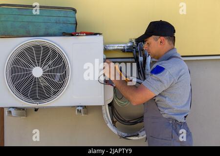 Bild eines Klempners mit Werkzeugen und eines Testers, der den Strom nach dem Einbau einer Klimaanlage in einem Haus überprüft Stockfoto