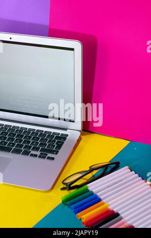 Schreibtisch mit Laptop und Markierungen auf farbidem Hintergrund Stockfoto