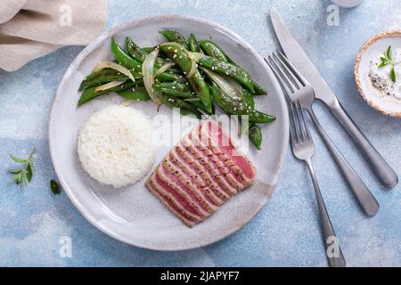 Gebratenes Thunfischsteak mit weißem Reis und grünen Erbsen Stockfoto