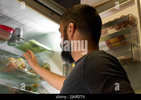 Blick von der Rückseite einer Person, die die Tür des Kühlschranks öffnet, um etwas im Inneren zu fangen Stockfoto