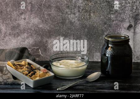 Glas mit natürlichem Honig und frisch zubereitetem hausgemachtem Joghurt neben einem Behälter mit Nüssen Stockfoto
