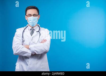 Männlicher Arzt in Maske, der im Studio auf die Kamera schaut Stockfoto