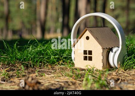 Miniatur-Sperrholzhaus mit kabellosen Kopfhörern im Wald. Ruhiges Haus auf dem Land. Stockfoto