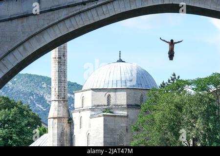 Mostar, Bosnien und Herzegowina – 2022. Mai: Mann taucht von der alten Brücke in Mostar 27 m hinunter in den Fluss Neretva. Brücke als Natio eingeschrieben Stockfoto
