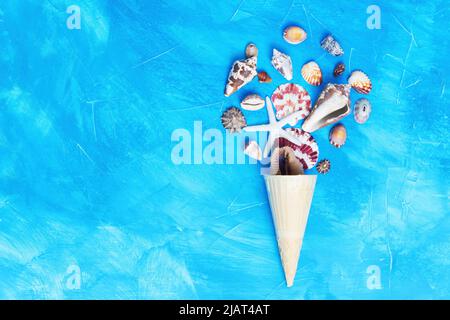 Eisform aus einem Waffelkegel und Muscheln auf blauem Hintergrund mit Kopierfläche. Stockfoto