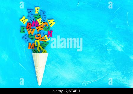 Eiscreme-Form aus einem Waffelkegel und einem Haufen von bunten Holzbuchstaben isoliert auf einem blauen texturierten Hintergrund mit Kopierraum. Kreative PR Stockfoto