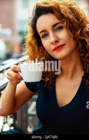 Junge marokkanerin mit lockigen braunen Haaren sitzt in einem Mainzer Café im Freien und trinkt Kaffee Stockfoto