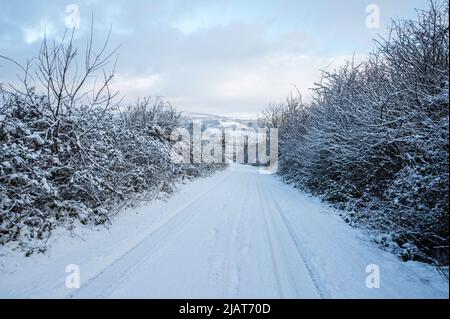 Eine mit Schnee bedeckte Landstraße am Morgen nach einem schweren Schneefall in South Wales, Großbritannien Stockfoto