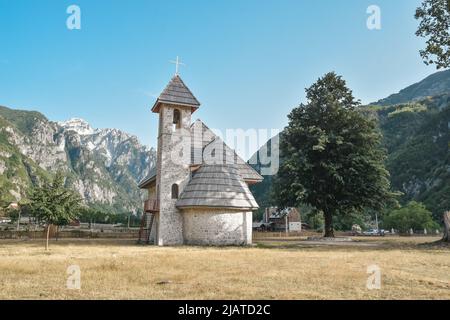 Ein Weg mit Holzzaun führt die katholische Kirche im Theth-Tal, im Hintergrund die Berge der albanischen Alpen Stockfoto