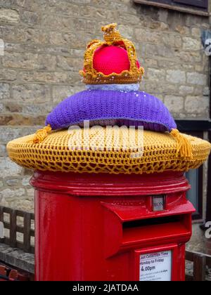 Royal Mail Postbox mit einem gestrickten Oberteil mit einer königlichen Krone zur Feier des Platinum Jubilee der Königin, Hackleton, Northamptonshire, Großbritannien Stockfoto