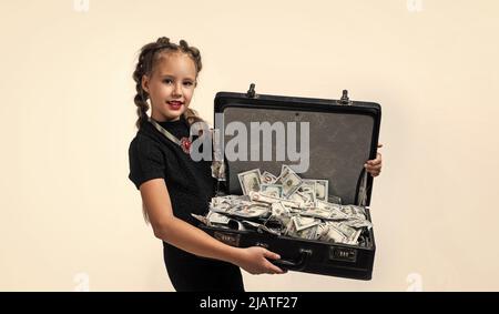 Hübsches Teenager-Mädchen mit Zöpfen hat viel Geld im Koffer isoliert auf weiß, Geld Stockfoto