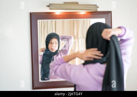 Spiegelung auf einem Wandspiegel einer muslimischen Frau, die ihren Kopftuch trägt. Stockfoto