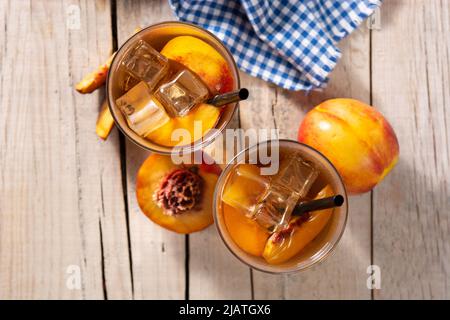 Glas Pfirsichtee mit Eiswürfeln auf Holztisch Stockfoto