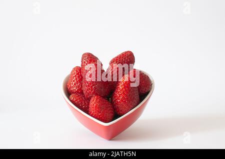 Natürliche rote Bio-Erdbeeren mit abgewinkelter Aussicht. Süße und köstliche Beeren in herzförmiger Schüssel, isoliert auf weißem Hintergrund, selektiver Fokus. Stockfoto