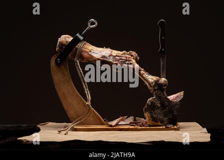 Jamon auf einem Holzständer zum Schneiden von Fleisch. Stück von Jamon auf Jamonero. Schinken, Jamon, Prosciutto. Studioaufnahme. Stockfoto